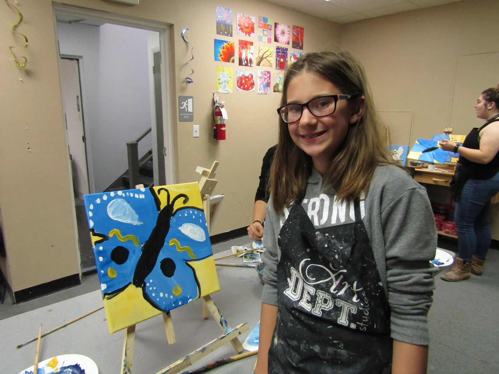 A smiling girl standing beside her butterfly painting